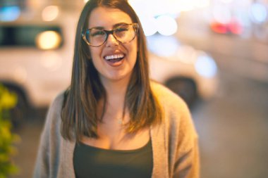 Mutlu ve kendinden emin gülümseyen genç ve güzel bir kadın. Kasaba caddesinde yüzünde gülümsemeyle dikilirken