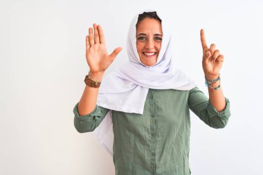 Geleneksel Müslüman tesettürlü genç, güzel bir Arap kadını izole edilmiş arka planda altı numaralı parmaklarıyla işaret ederken kendinden emin ve mutlu bir şekilde gülümsüyor..