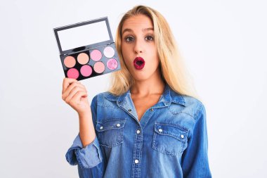 Güzel, sarışın bir kadın makyajını yalnız beyaz arka plan üzerinde yapıyor. Şaşırmış bir yüzle korkmuş ve korku ifadesinden heyecanlanmış.