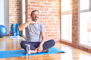 Orta yaşlı yakışıklı sporcu mindere oturmuş yoga egzersizi yapıyor spor salonunda boğazını bıçak gibi kesiyor, saldırganlığı şiddet ile tehdit ediyor.