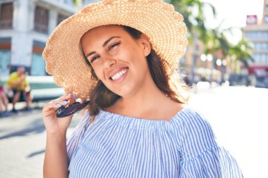 Genç ve güzel bir kadın mutlu bir şekilde gülümsüyor güneşli bir yaz gününde şehir sokaklarında yürüyor.