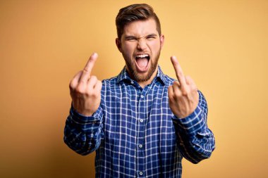Sarışın, sakallı ve mavi gözlü genç bir işadamı sarı arka planda tişört giyiyor orta parmağının kötü ifadesini, provokasyonunu ve kaba davranışını gösteriyor. Heyecanlı çığlık