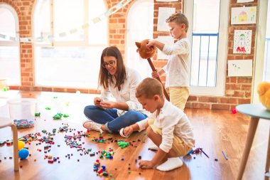 Güzel öğretmen ve yeni yürümeye başlayan çocuklar anaokulunda bir sürü oyuncakla oynuyorlar.