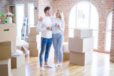 Genç güzel çift karton kutular etrafında yeni evde kahve fincan içme ayakta