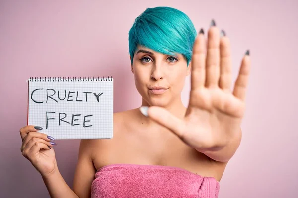 Young woman with blue fashion hair showing cruelty-free cosmetics message with open hand doing stop sign with serious and confident expression, defense gesture