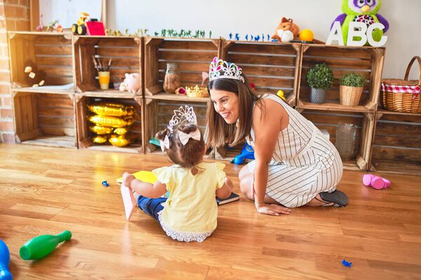 Young beautiful teacher and toddler wearing princess crown at kindergarten