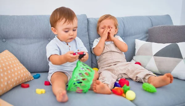 Belas Crianças Uma Delas Chorando Sentada Sofá Brincando Com Brinquedos — Fotografia de Stock