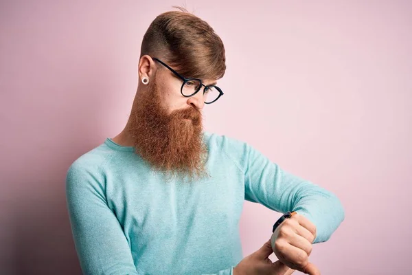 ハンサムなアイルランドの赤毛男とともに髭を身に着けています眼鏡上ピンク隔離された背景手首の時計で時間を確認します リラックスして自信を持って — ストック写真