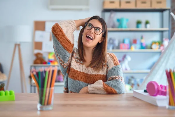 Ung Vakker Lærerkvinne Med Genser Briller Sittende Pulten Barnehagen Smilende – stockfoto