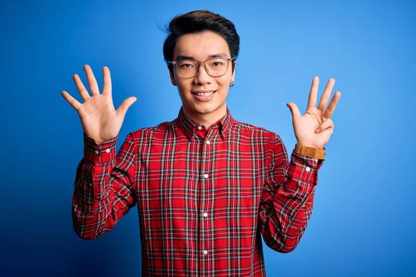 若いですハンサムな中国人男性身に着けていますカジュアルシャツと眼鏡上の青の背景ショーと指差し込みで指番号9ながら笑顔自信と幸せ — ストック写真
