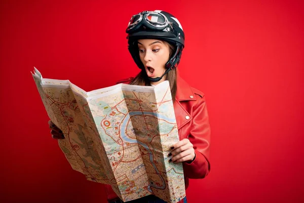 Young beautiful tourist motorcyclist woman wearing motorcycle helmet holding city map scared in shock with a surprise face, afraid and excited with fear expression