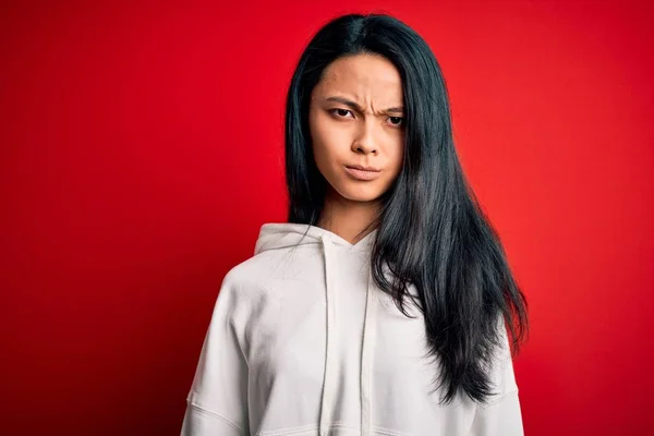 Young beautiful chinese sporty woman wearing sweatshirt over isolated red background skeptic and nervous, frowning upset because of problem. Negative person.