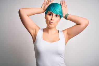 Mavi saçlı, beyaz arka plan üzerine günlük tişört giyen, avuçlarında alaycı ve şüpheci el hareketleriyle tavşan kulağı hareketi yapan genç ve güzel bir kadın. Paskalya tavşanı kavramı.