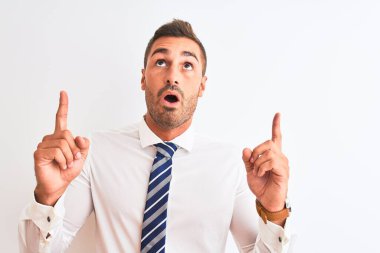 Young handsome elegant business man over isolated background amazed and surprised looking up and pointing with fingers and raised arms.