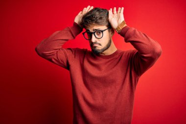 Sakallı, gözlüklü ve süveterli genç bir adam kırmızı arka planda dikiliyor. Tavşan kulakları hareketi yapıyor. Avuçlarında alaycı ve şüpheci bakışlar var. Paskalya tavşanı kavramı.