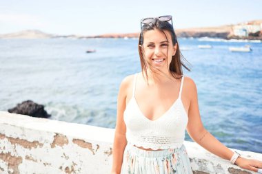 Güzel genç bir kadın kumsalda yürüyor okyanus manzarasının tadını çıkarıyor yaz tatilinde gülümsüyor.