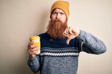Kızıl saçlı, sakallı, kış şapkalı, sıcak kahve içen kızgın yüzlü, olumsuz işaretli baş parmaklı, reddedilme konsepti olan İrlandalı bir adam.