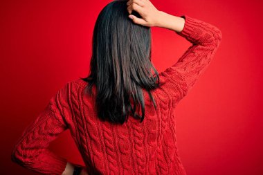 Young brunette woman with blue eyes wearing casual sweater over isolated red background Backwards thinking about doubt with hand on head