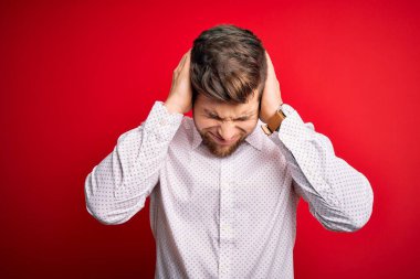 Sarışın, sakallı ve mavi gözlü genç bir işadamı kırmızı arka plan üzerinde şık bir gömlek giyiyor. Ağrı ve migren yüzünden çaresiz ve stresli. Ellerini başının üstüne koy..