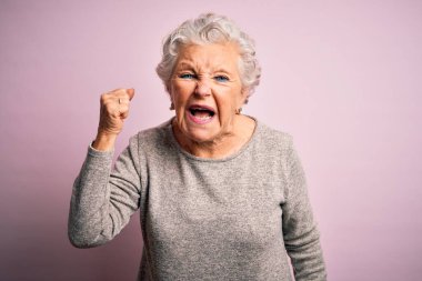 Son sınıf güzeli, rahat bir tişört giymiş, pembe arka planda dikiliyor kızgın ve kızgın bir şekilde yumruğunu kaldırıyor ve öfkeyle bağırıyor. Öfke ve agresif kavram.