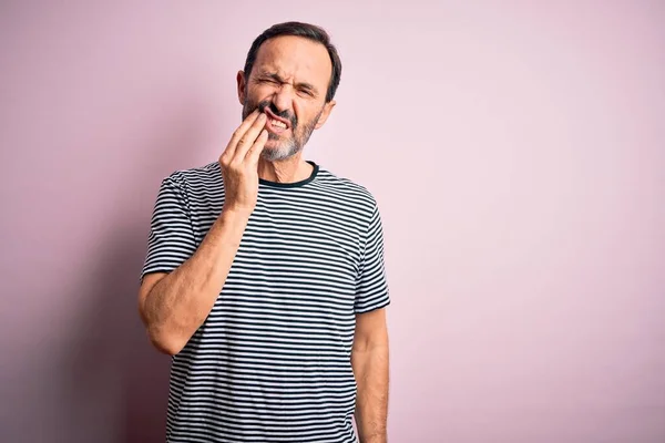 歯の痛みや歯の病気のために痛みを伴う表現で手で手に触れる孤立したピンクの背景の上に立ってカジュアルな縞模様のTシャツを身に着けている中年の蜂蜜の男 歯医者 — ストック写真