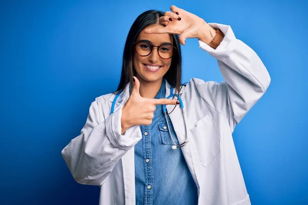 青い背景に聴診器と眼鏡をかけた若い美医師の女性が 笑顔で手や指でフレームを作っています 創造性と写真の概念 — ストック写真