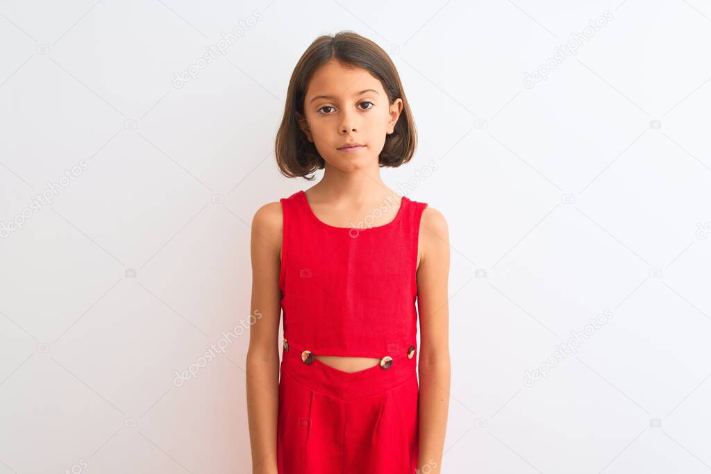 Young beautiful child girl wearing red casual dress standing over isolated white background with serious expression on face. Simple and natural looking at the camera.