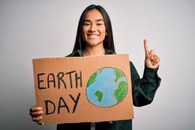 Genç ve güzel Asyalı bir kadın elinde bayrak tutarak toprak ve çevre koruma istiyor. Bir fikir ya da soruyla şaşırmış ve mutlu bir yüzle işaret ediyor.