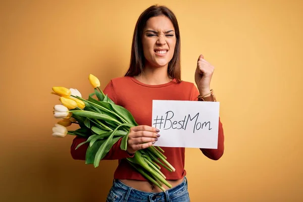 Beautiful woman celebrating mothers day holding best mom message and bouquet of tulips annoyed and frustrated shouting with anger, crazy and yelling with raised hand, anger concept