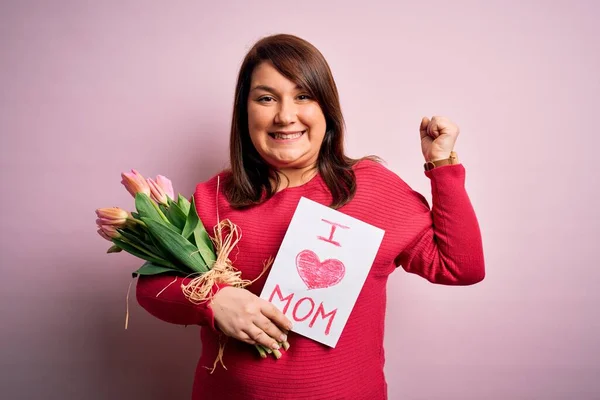 Beautiful plus size woman celebrating mothers day holding message and bouquet of tulips screaming proud and celebrating victory and success very excited, cheering emotion