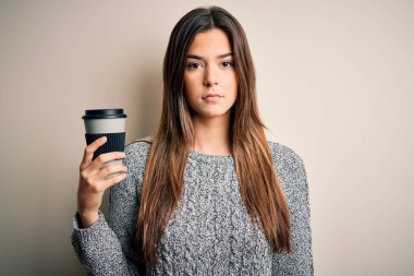 Genç, güzel bir kız, izole edilmiş beyaz arka planda duran bir fincan kahve içiyor. Zeki bir yüz ifadesiyle ciddi olduğunu düşünüyor.