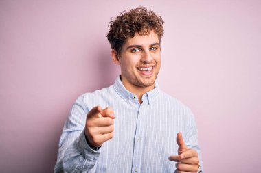 Sarışın, kıvırcık saçlı, beyaz arka planda çizgili gömlek giyen, mutlu ve komik yüzlü genç bir adam. İyi enerji ve titreşimler.