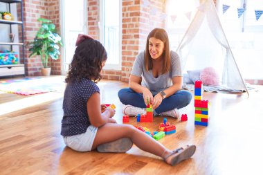 Güzel öğretmen ve küçük kız anaokulunda inşaat bloklarıyla oynuyorlar.