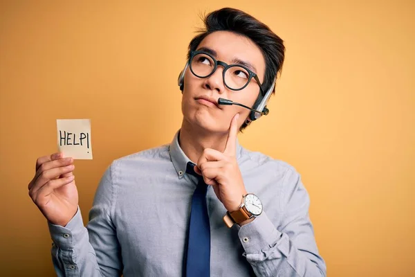 Young handsome chinese call center agent man overworked using headset asking for help serious face thinking about question, very confused idea