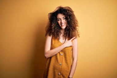 Güzel esmer kadın tatilde. Kıvırcık saçlı, piercing 'li, şapkalı, neşeli elbiseli. Yüzünde mutlu ve doğal bir ifade var.