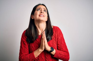 Young brunette woman with blue eyes wearing casual sweater over isolated white background begging and praying with hands together with hope expression on face very emotional and worried. Begging.