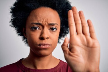 Beyaz arka planda duran kıvırcık saçlı, güzel Afro-Amerikan kadın. Eli açık, dur işareti yapıyor. Ciddi ve kendinden emin bir ifadeyle, savunma hareketi yapıyor.