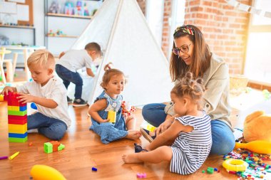 Güzel öğretmen ve bir grup çocuk anaokulunda bir sürü oyuncakla oynuyorlar.
