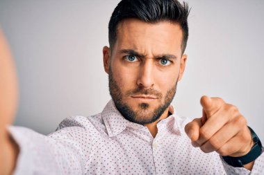 Genç, yakışıklı bir adam kameranın önünde özçekim yaparken beyaz arka planda parmağıyla kamerayı işaret ediyor ve sen, el işareti, ön taraftan pozitif ve kendinden emin bir hareket.