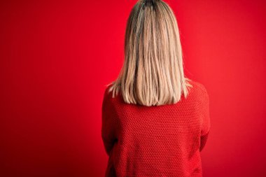 Young beautiful blonde woman wearing casual sweater over red isolated background standing backwards looking away with crossed arms
