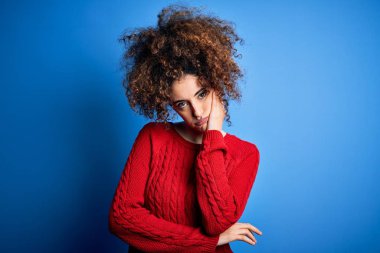 Kıvırcık saçlı ve piercing giyen genç bir kadın kollarını kavuşturup depresyondan sıkılmış ve yorgun gözüktüğünü düşünüyor..