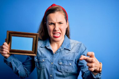 Güzel, sarışın bir kadın, mavi arka plan üzerinde klasik çerçeveler tutuyor. Öfkeyle bağırıyor, çıldırıyor ve öfkeyle bağırıyor.