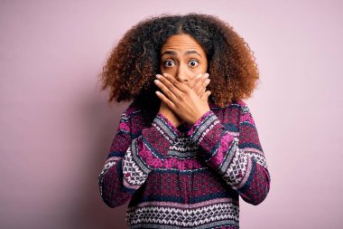 Young african american woman with afro hair wearing colorful shirt over pink background shocked covering mouth with hands for mistake. Secret concept.