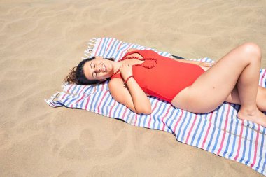 Genç ve güzel bir kadın havlunun üzerinde güneşleniyor ve maspalomas kumullarında eşofman giyiyor.