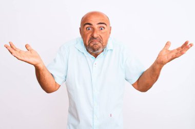 İzole edilmiş beyaz arka plan üzerinde dikilen orta yaşlı, yakışıklı bir adam. Kolları ve elleri havada, kafası karışmış bir ifade. Şüphe kavramı.