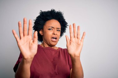 Young beautiful African American afro woman with curly hair wearing casual t-shirt standing afraid and terrified with fear expression stop gesture with hands, shouting in shock. Panic concept.