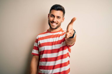 Sıradan çizgili tişört giyen yakışıklı genç bir adam izole edilmiş beyaz arka planda durup dostça gülümseyerek selamlama ve hoş geldin diyor. Başarılı bir iş..