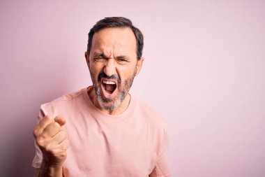 Middle age hoary man wearing casual t-shirt standing over isolated pink background angry and mad raising fist frustrated and furious while shouting with anger. Rage and aggressive concept.