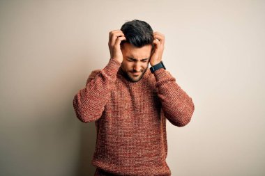 Young handsome man wearing casual sweater standing over isolated white background suffering from headache desperate and stressed because pain and migraine. Hands on head.
