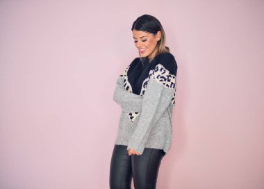 Şık kıyafetler giyen, mutlu ve kendinden emin gülümseyen genç ve güzel bir kadın. İzole edilmiş pembe arka planda yüzünde bir gülümsemeyle duruyorum.